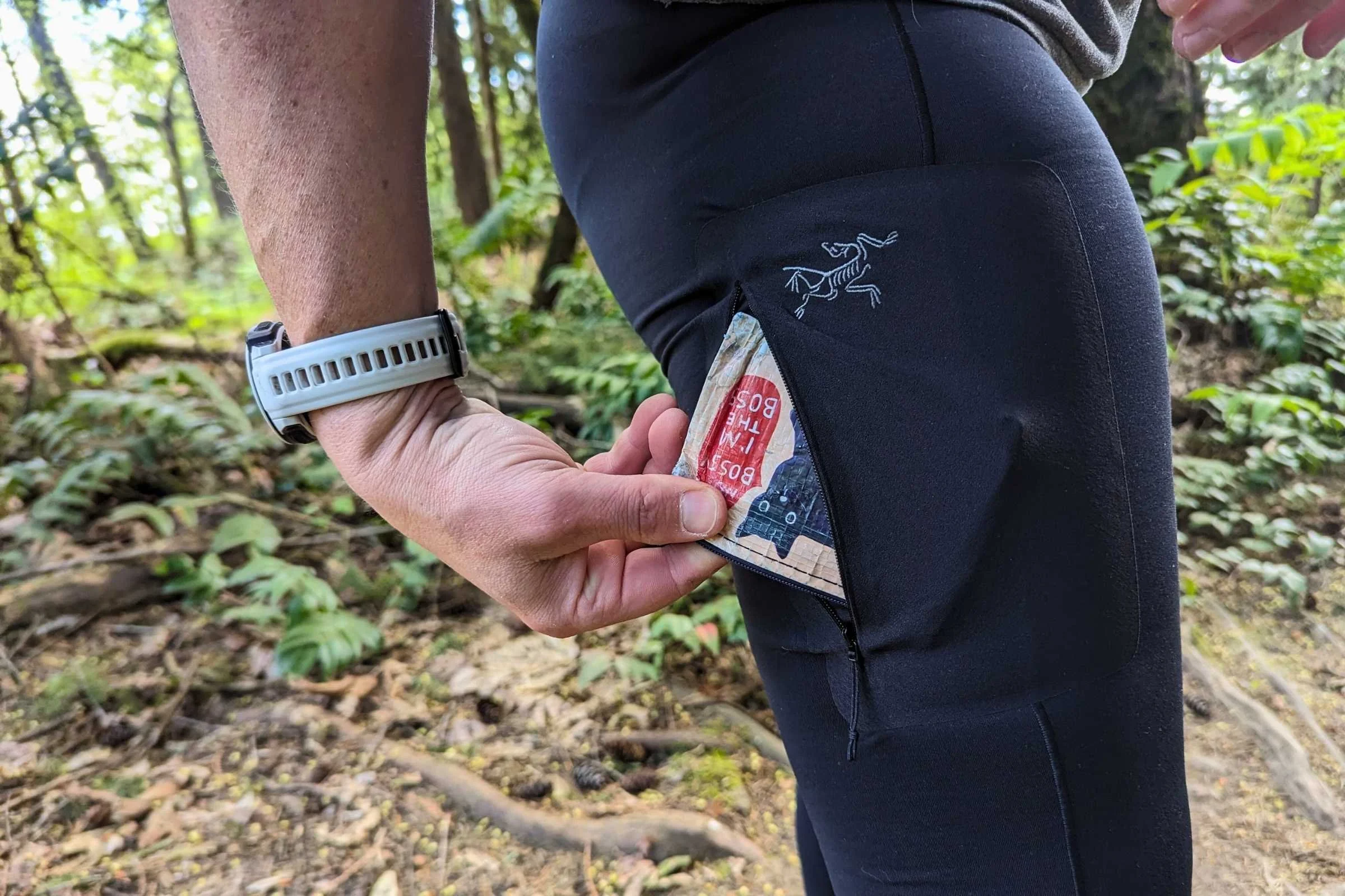 Detailed view of a small zippered pocket on the thigh of a black pair of leggings.