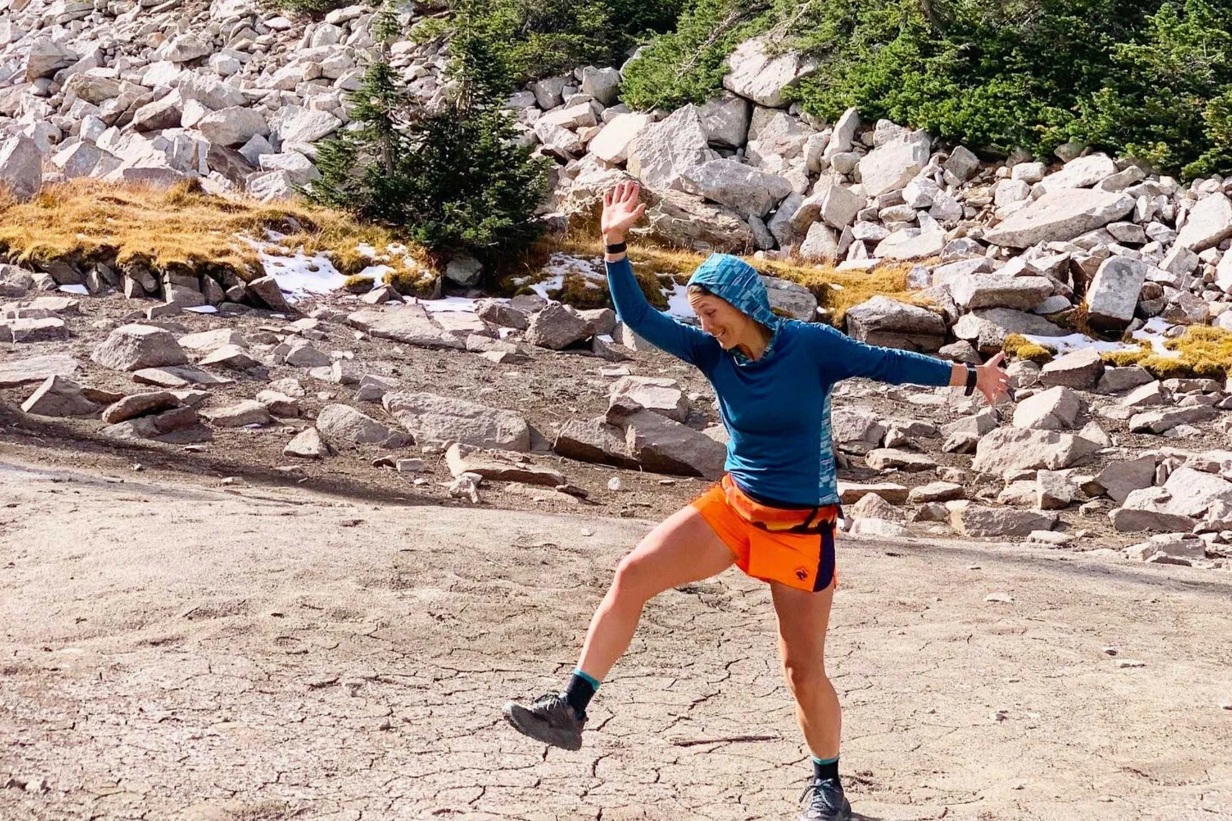 A woman trail running through a forest wearing a purple Smartwool base layer hoody.