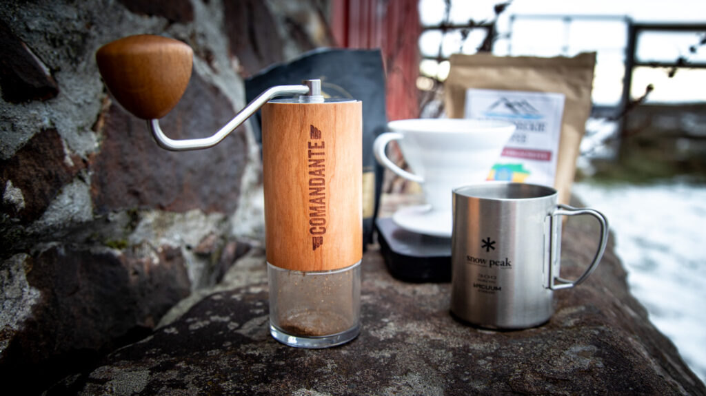 A Comandante C40 manual coffee grinder being used in an outdoor setting.