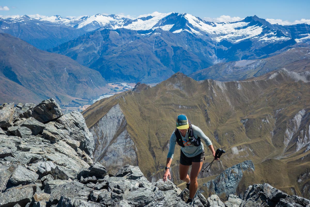 A female runner wearing a hydration pack while climbing a steep mountain ridge.