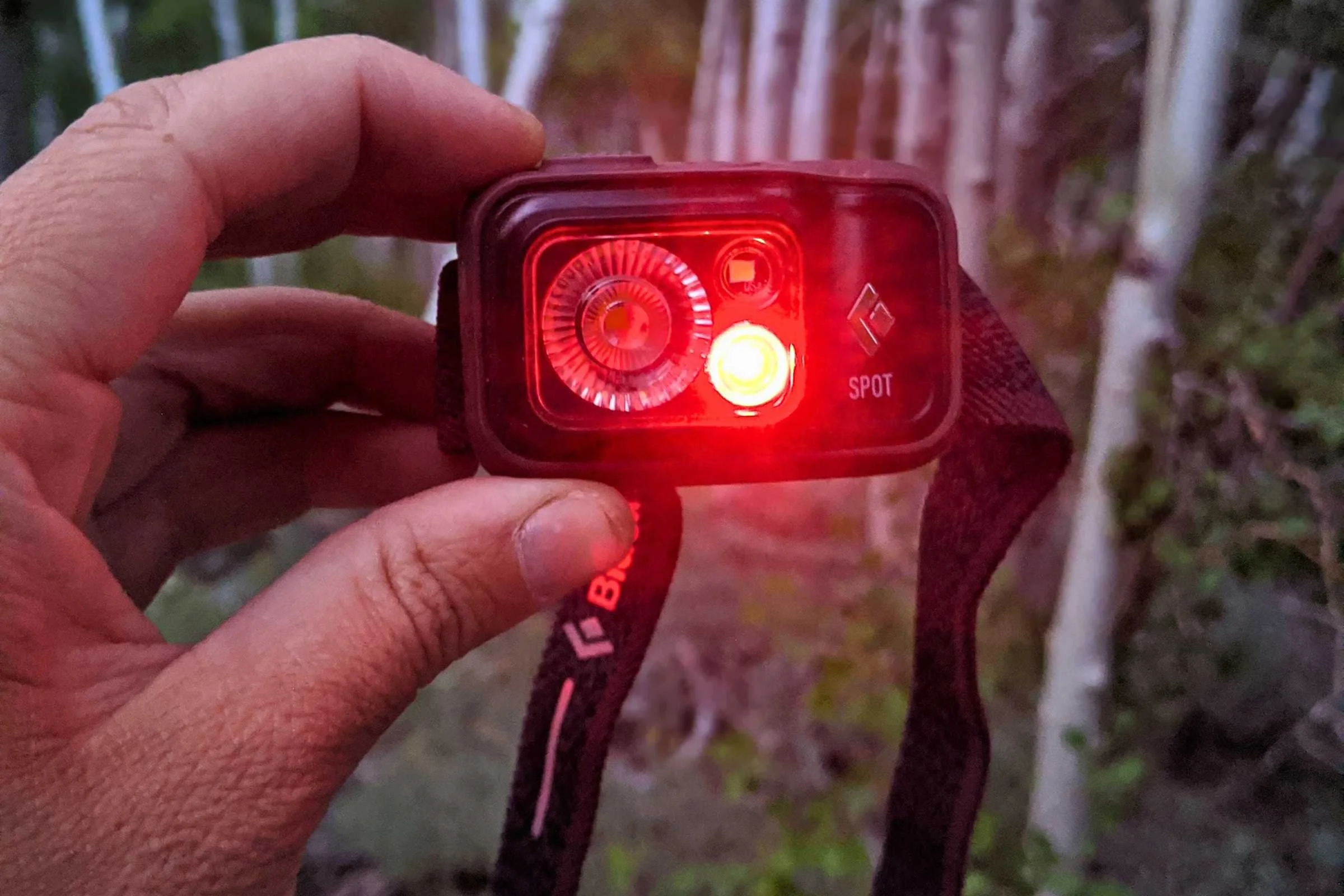 A close-up of the Black Diamond Spot 400 emitting a red light in a dark camping environment.