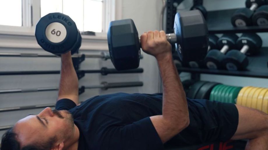 A man performing a chest press using professional-grade Eleiko dumbbells.