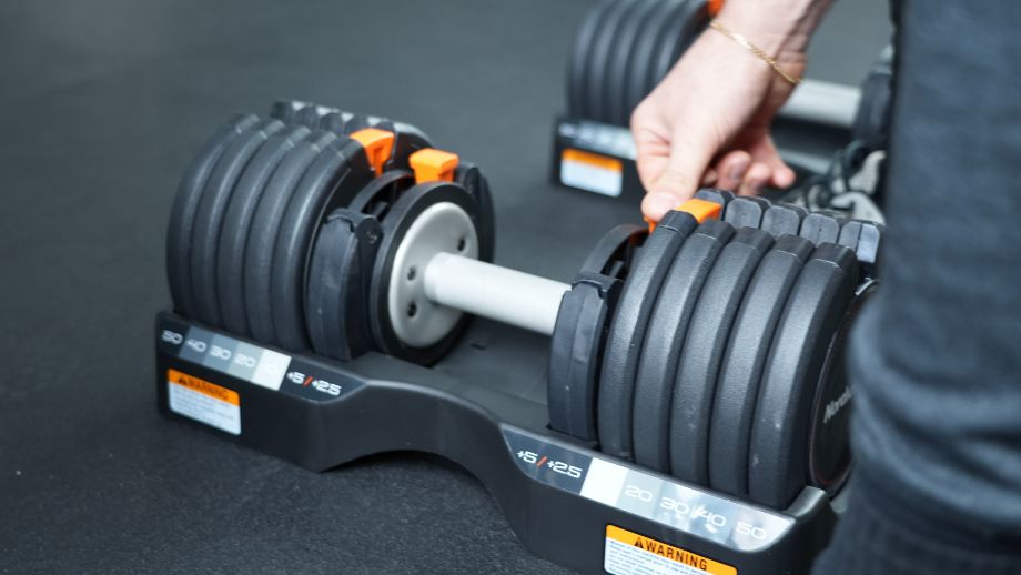 Close-up of a hand adjusting the weight dial on a selectorized adjustable dumbbell.