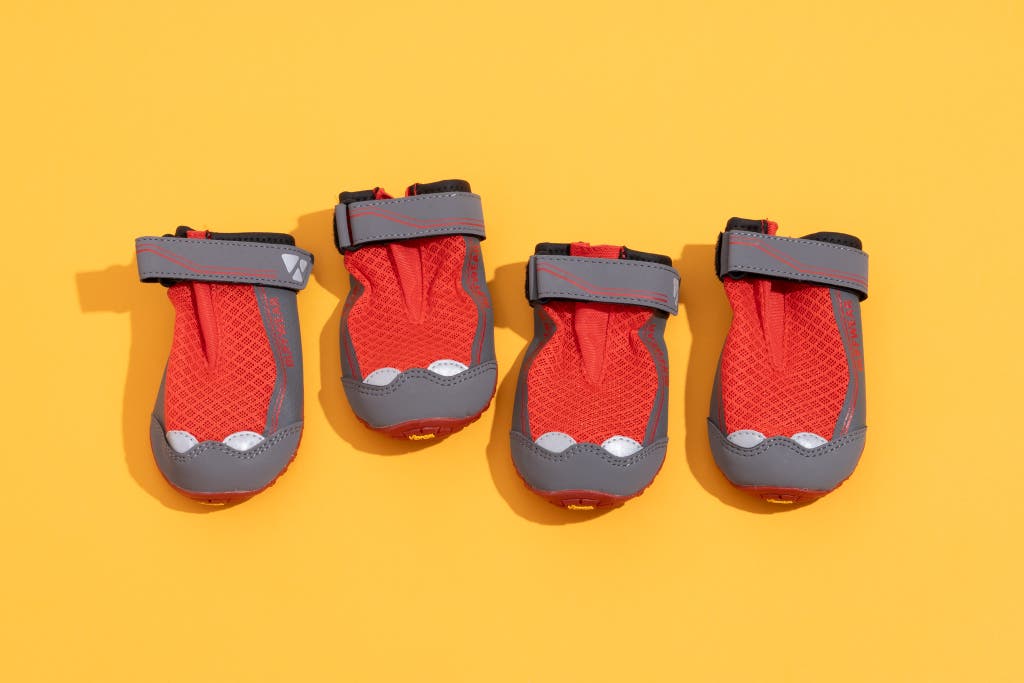 Four red and grey Ruffwear Grip Trex dog boots arranged on a yellow background.