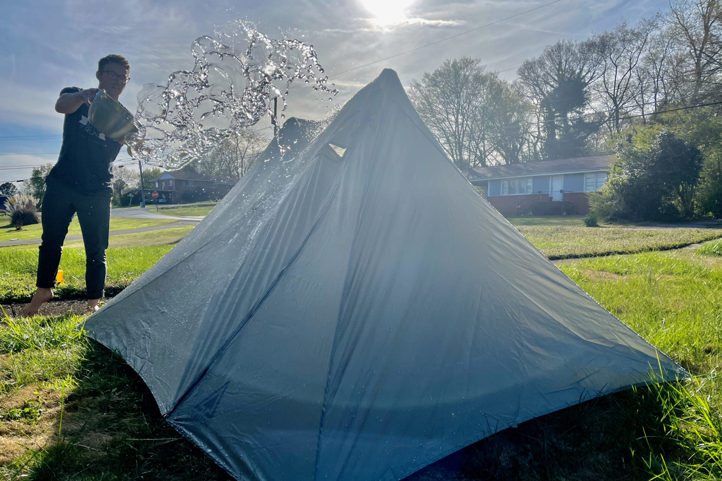 A person using a high-pressure garden hose to spray a Durston X-Mid tent to test seam sealing and waterproofness.
