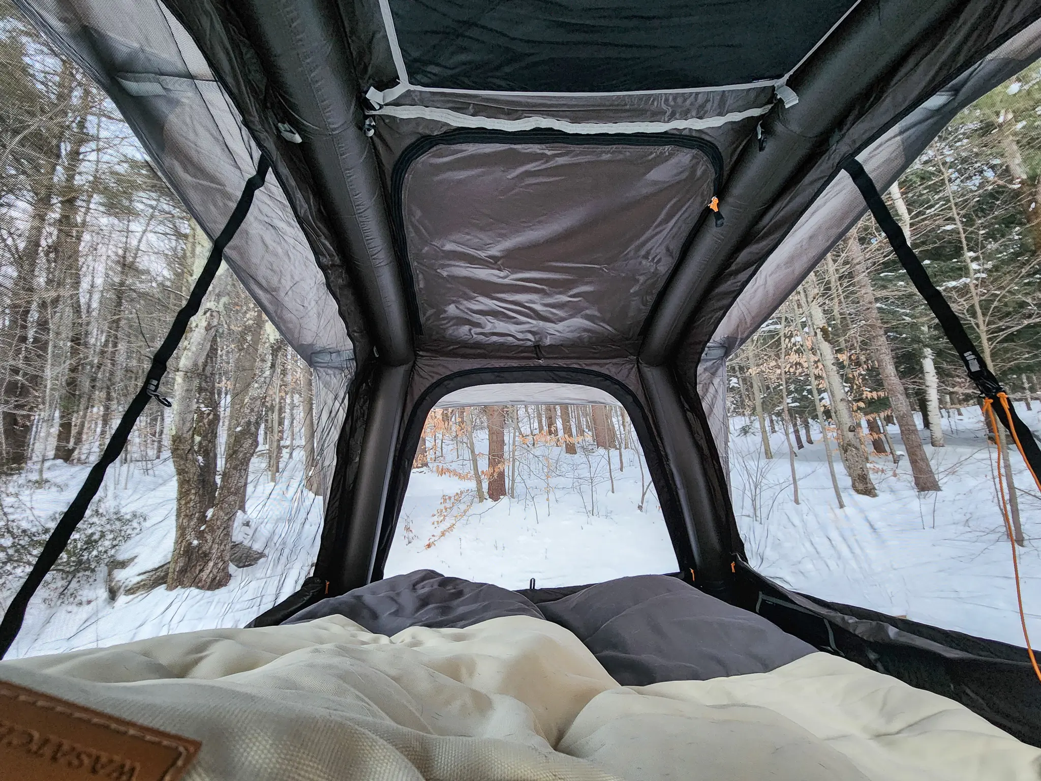 Wide-angle view of a rooftop tent interior featuring a thick foam mattress and organized sleeping gear.