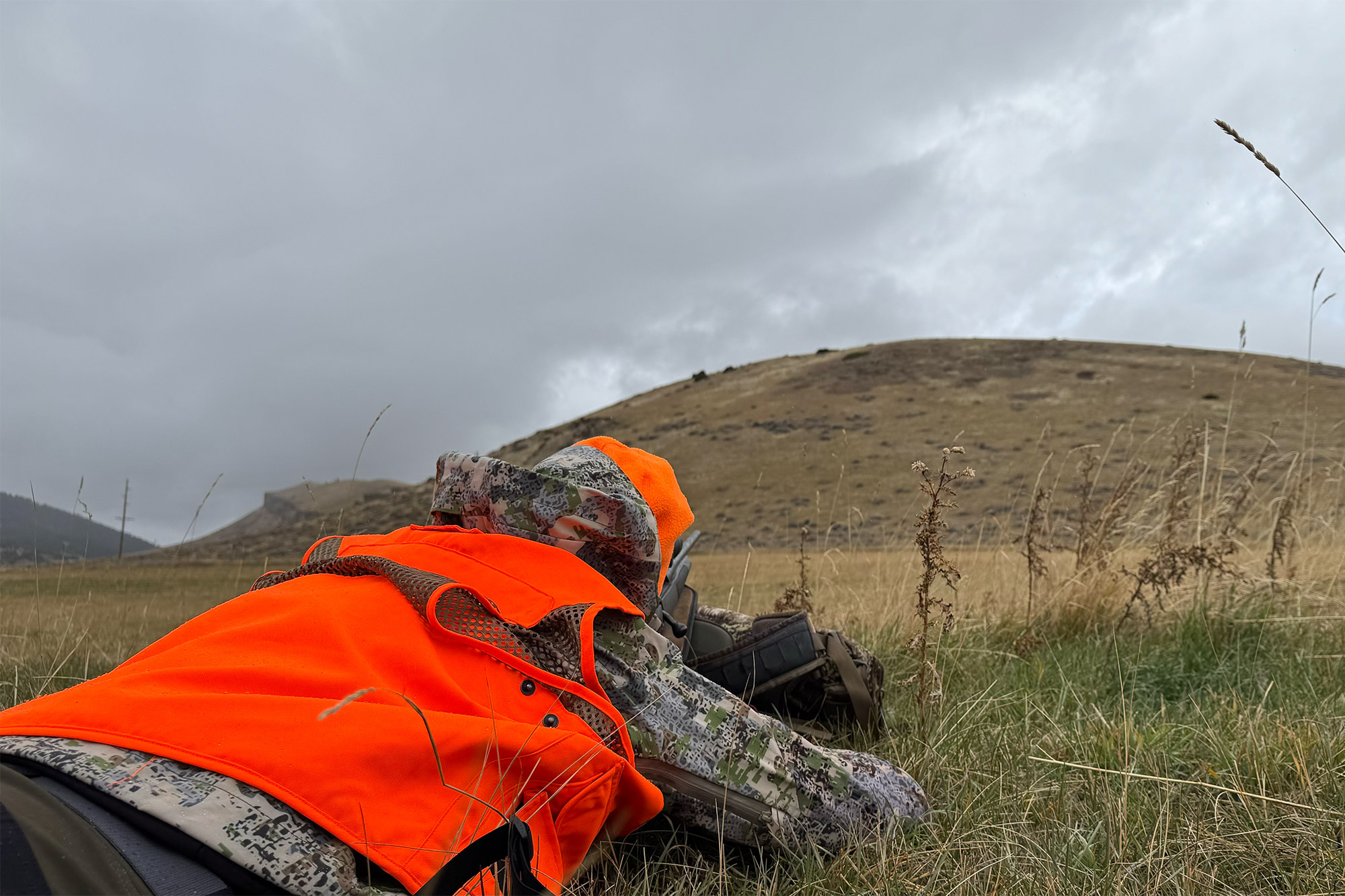 A hunter wearing the AllClima jacket lying face down in wet, green grass.