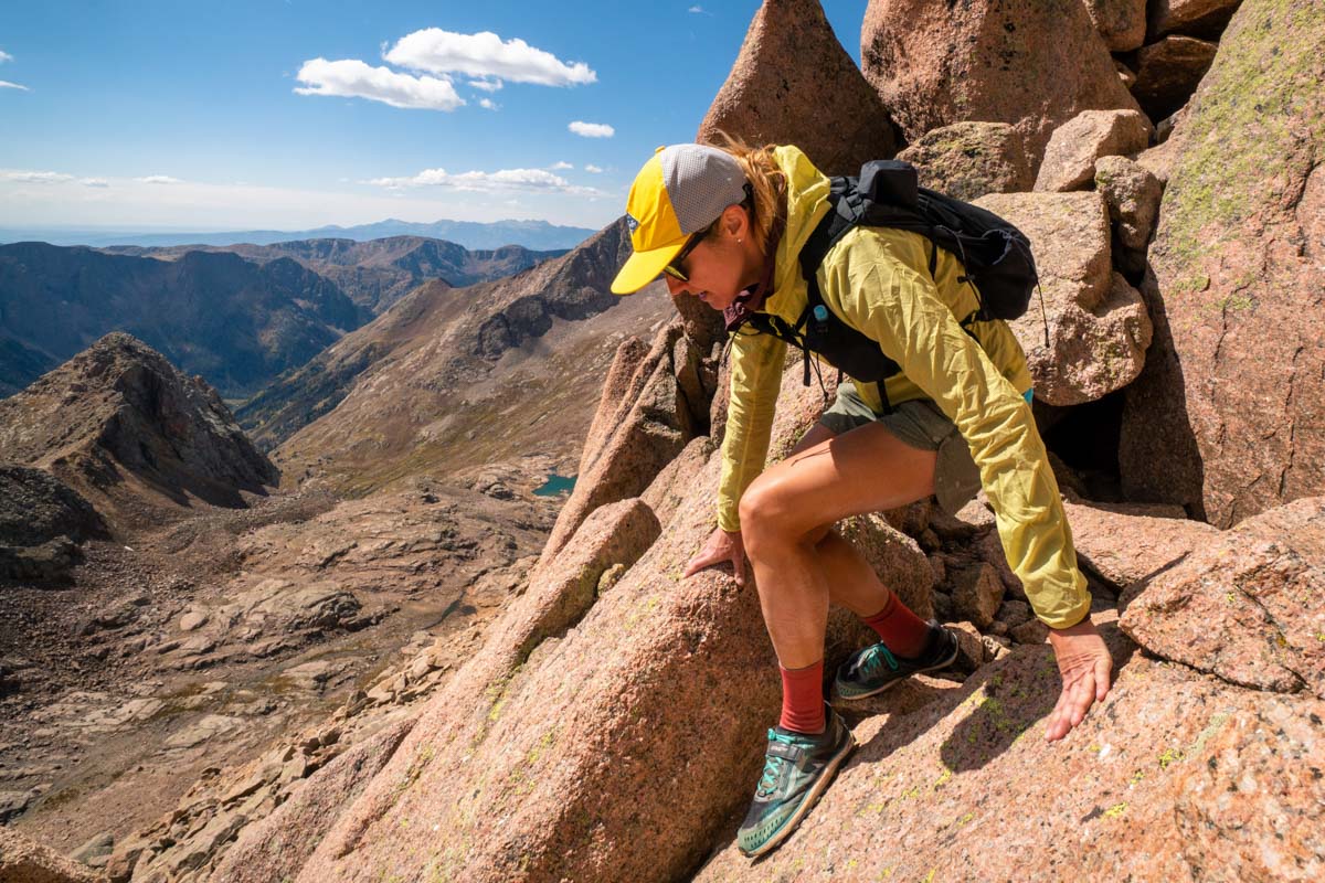 A runner scrambling on rocky, technical terrain wearing a durable hydration pack.