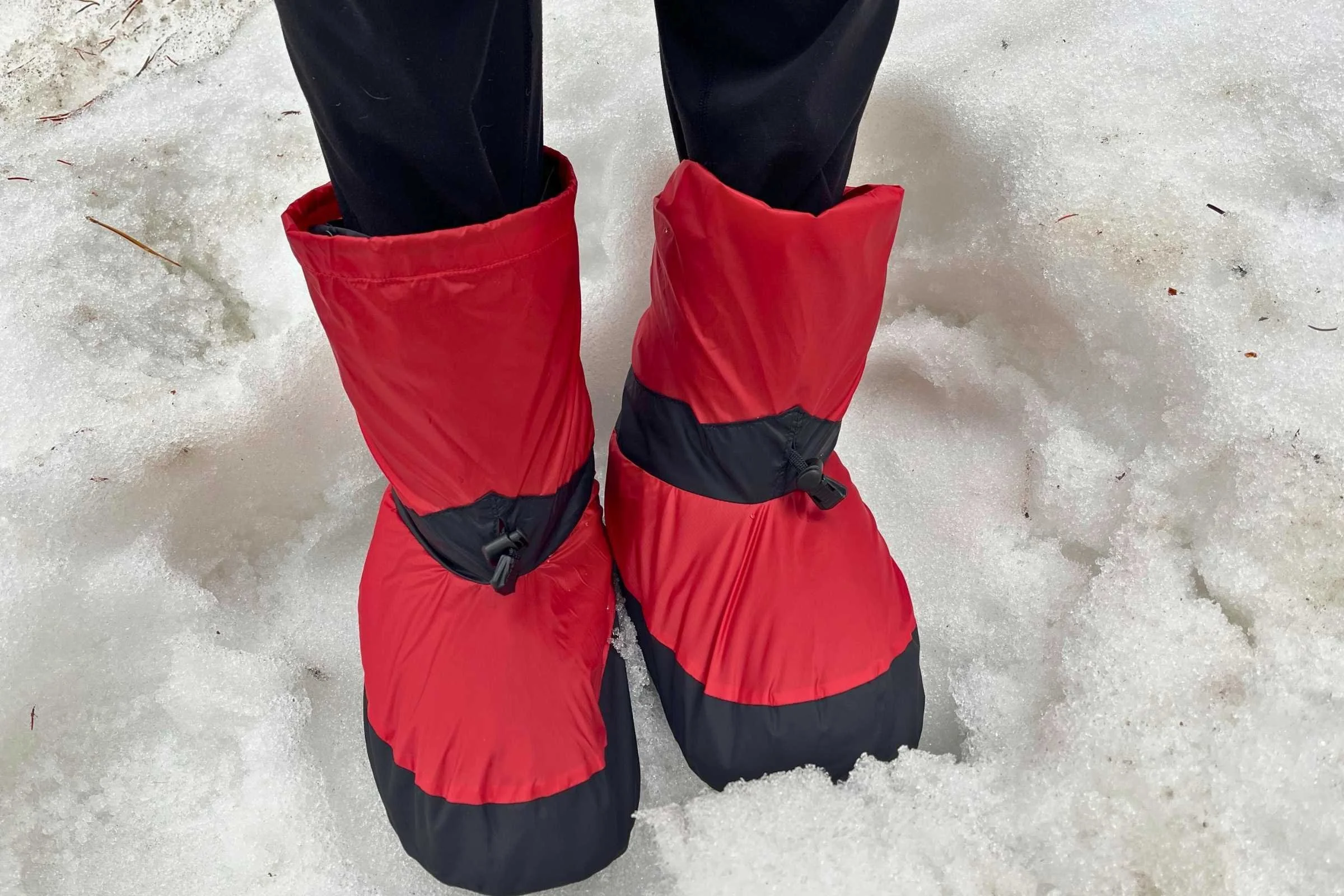 Light blue down-filled booties with a protective outer shell sitting on a snowy surface.
