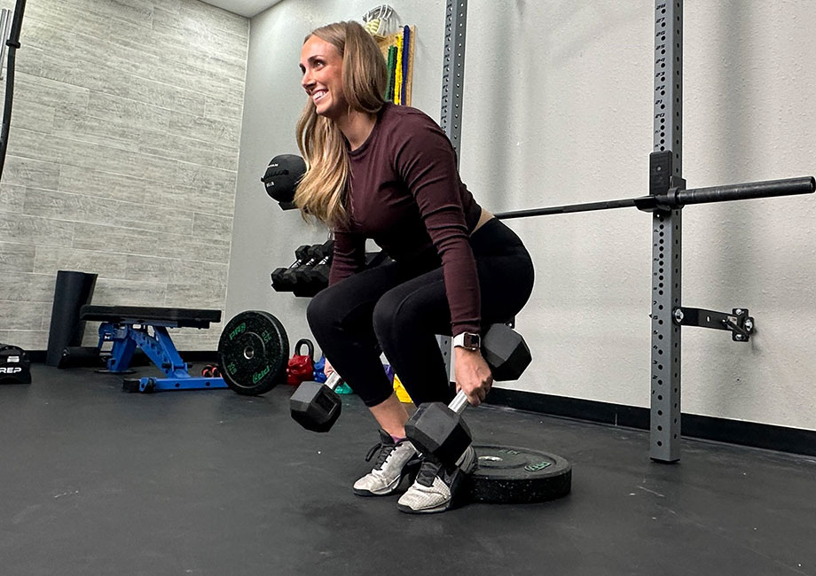 Woman holding dumbbells while performing a heels-elevated hack squat.