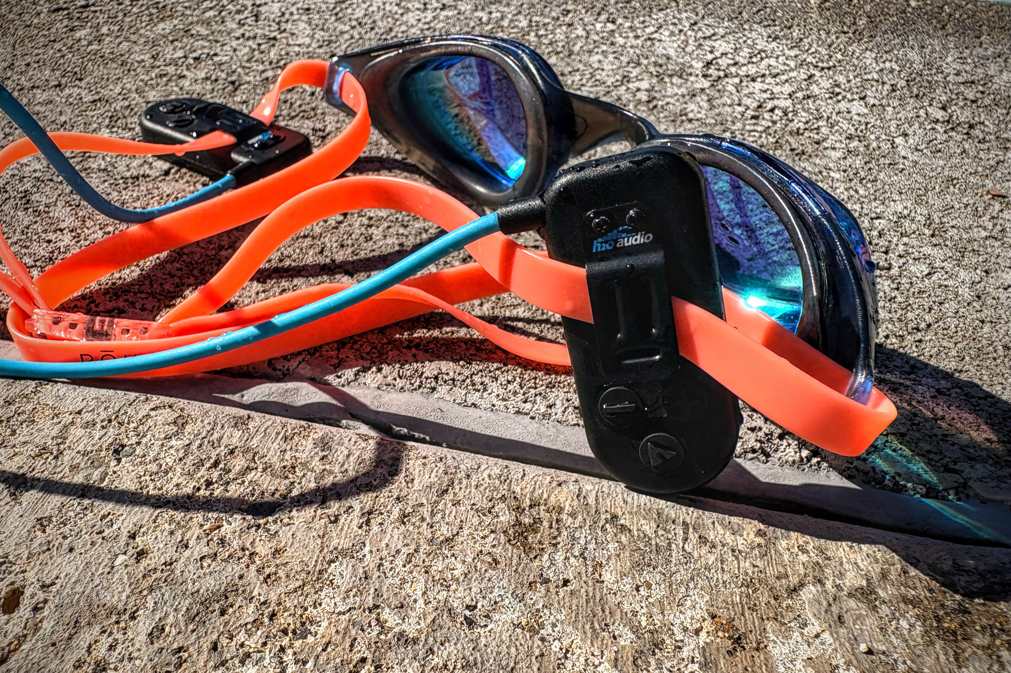 Detailed close-up of the H2O Audio Sonar 2 Pro device clipped onto the black silicone strap of swimming goggles.