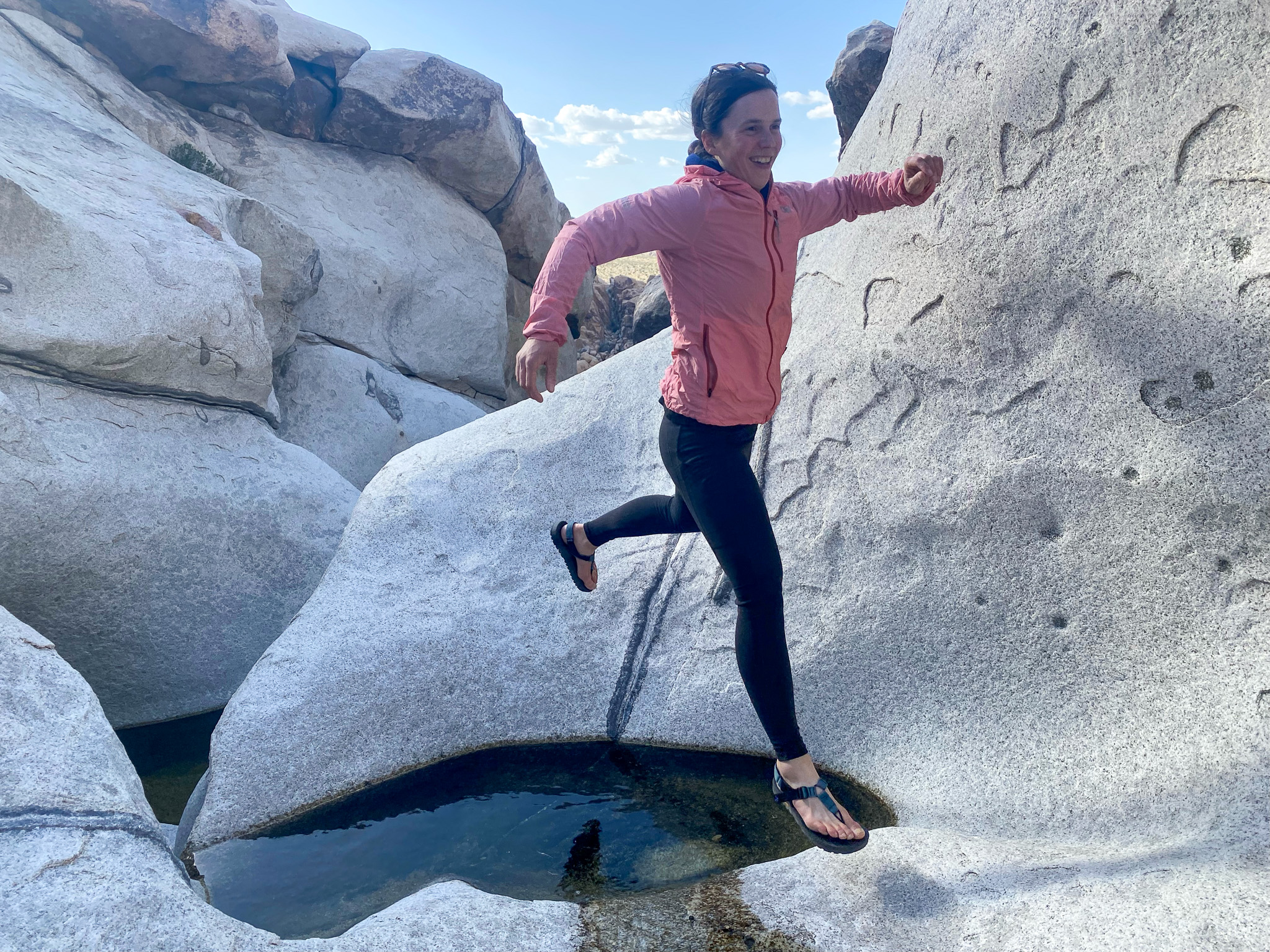 A female hiker leaping across a water gap in a rocky canyon.