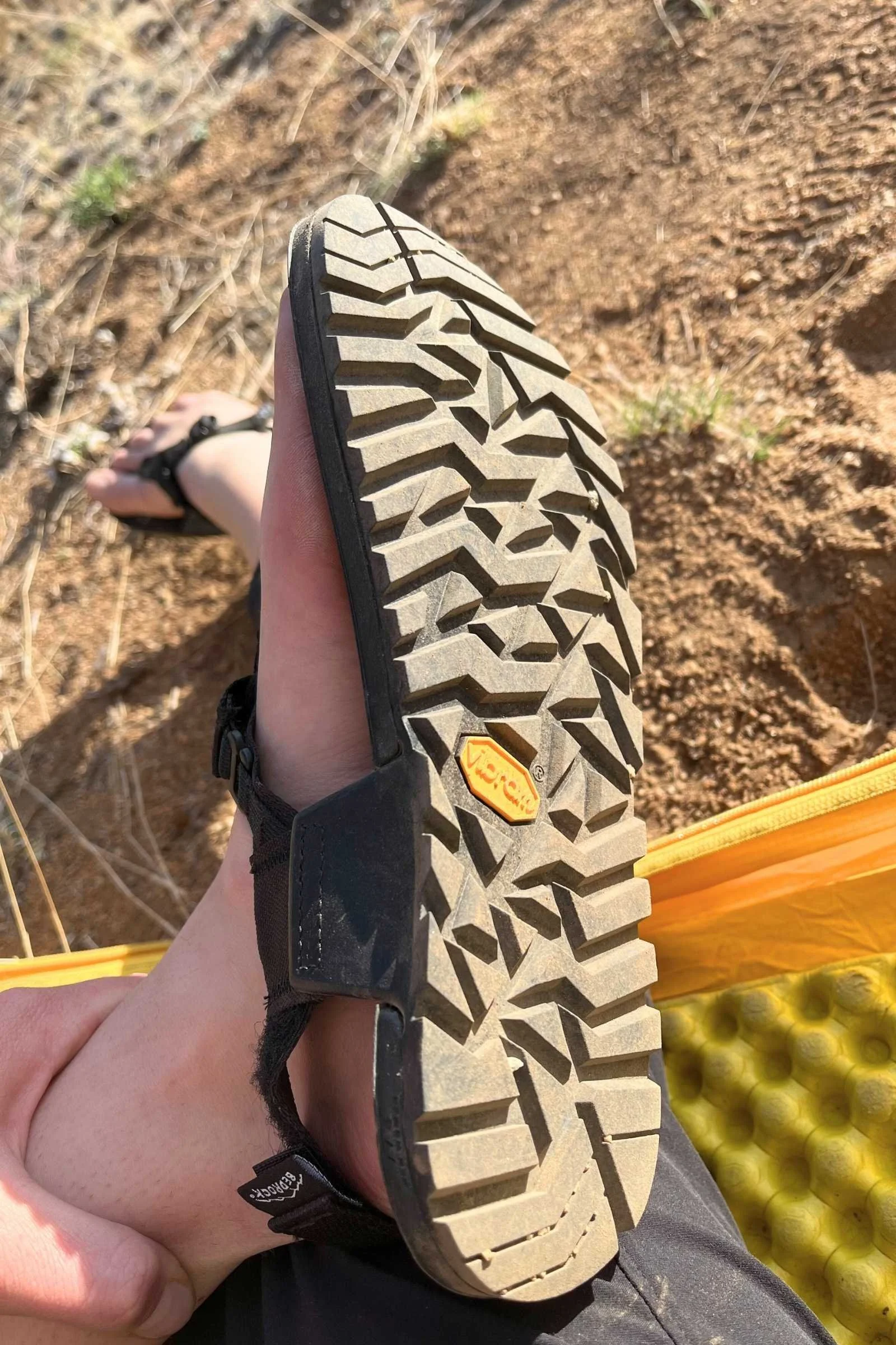 Detailed close-up of the rugged yellow Vibram logo and lugs on the bottom of a sandal.