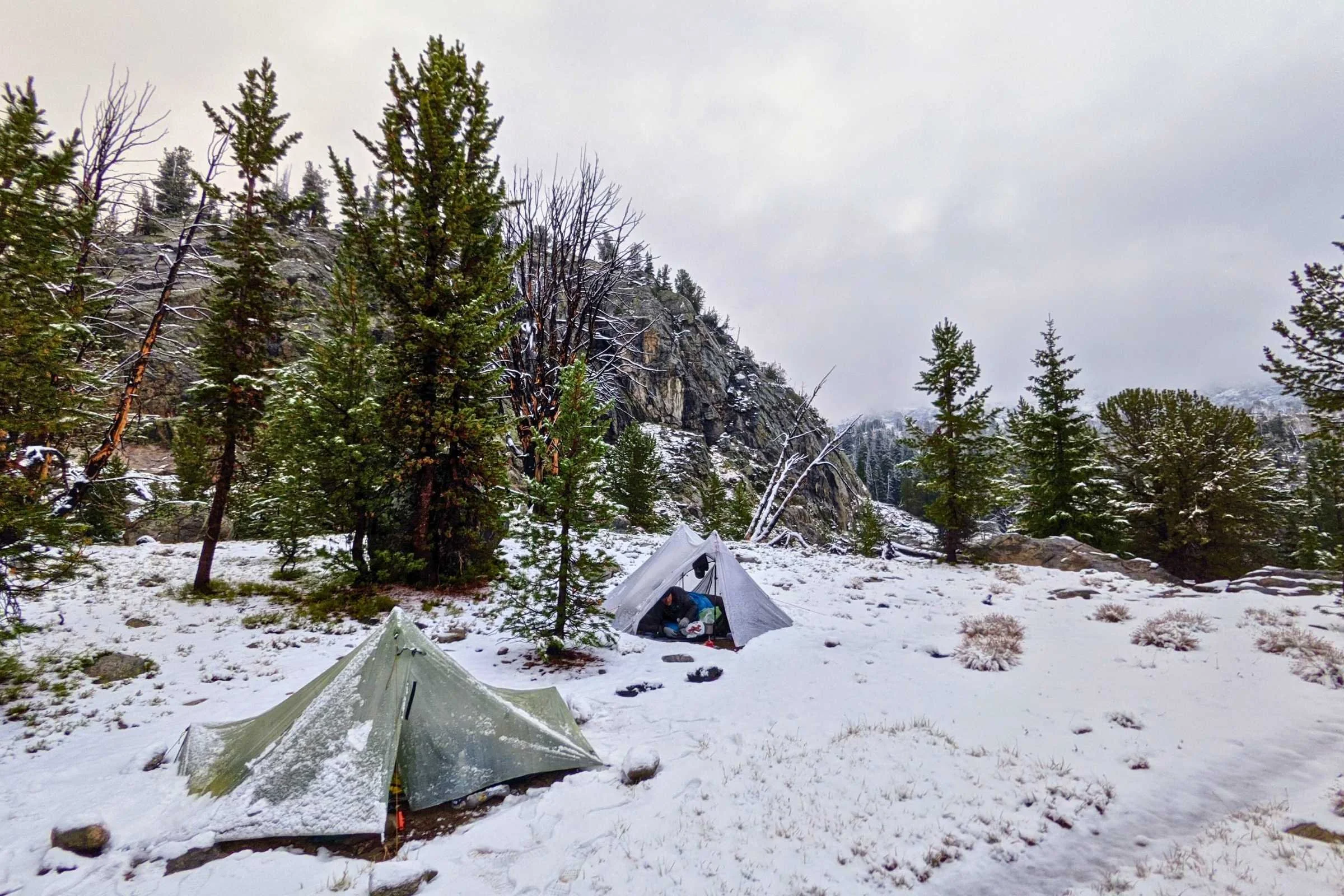 A Tarptent Aeon Li solo tent standing in a light dusting of snow with mountains in the background.