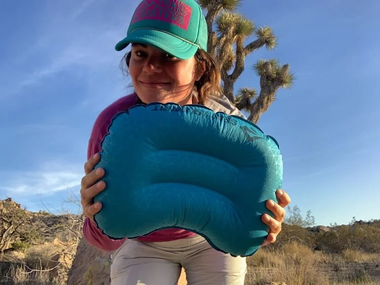 A person holding the compact Sea to Summit Aeros Ultralight pillow against a natural outdoor background.