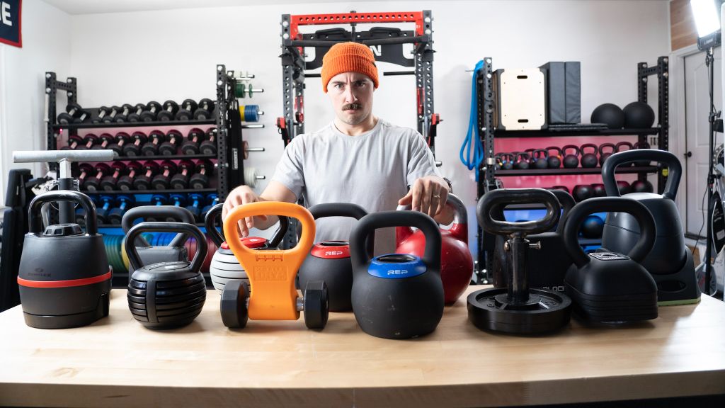Person posing with a collection of different kettlebells.
