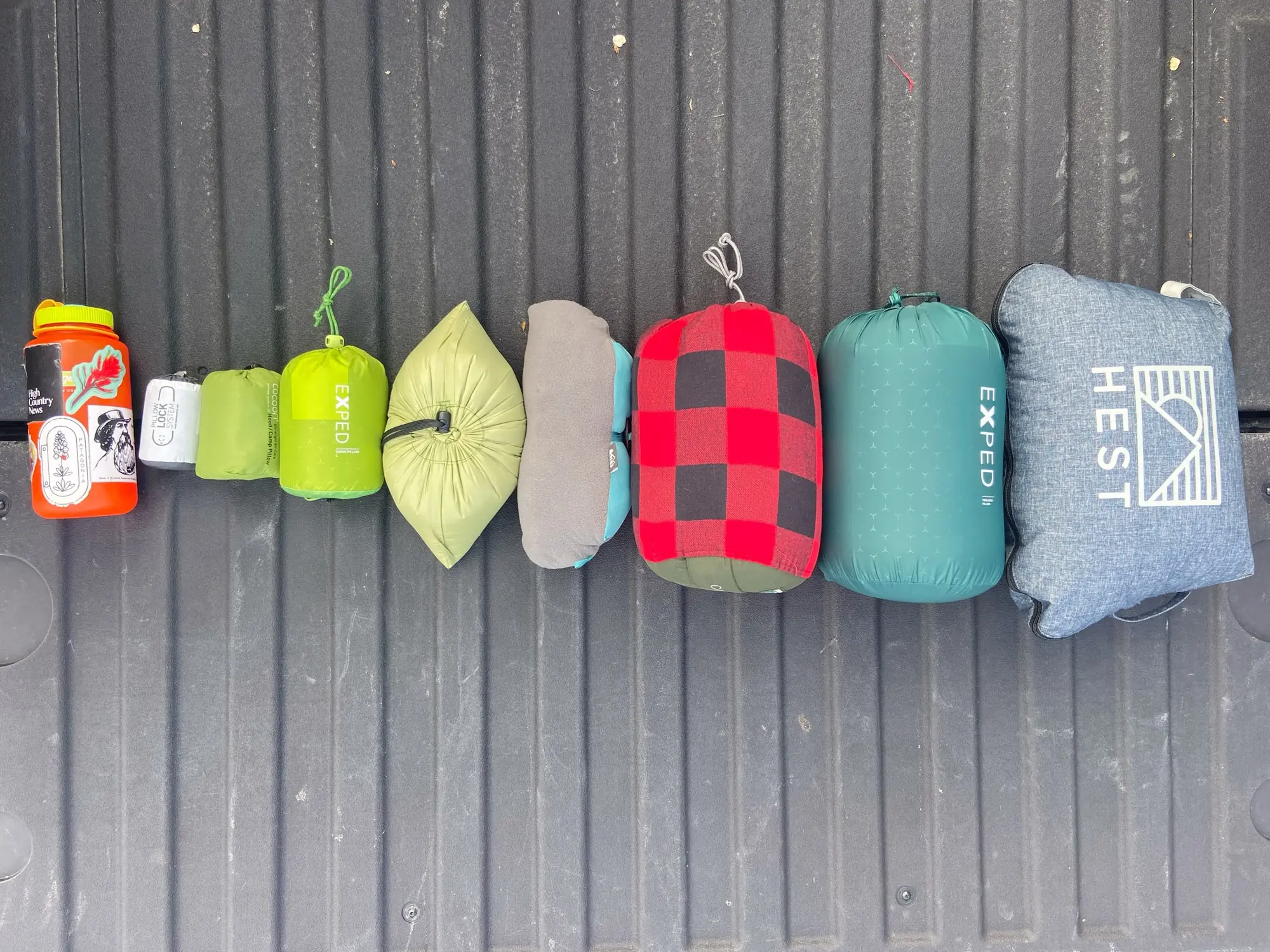 Several backpacking pillows packed into their respective stuff sacks sitting side-by-side to show size differences.