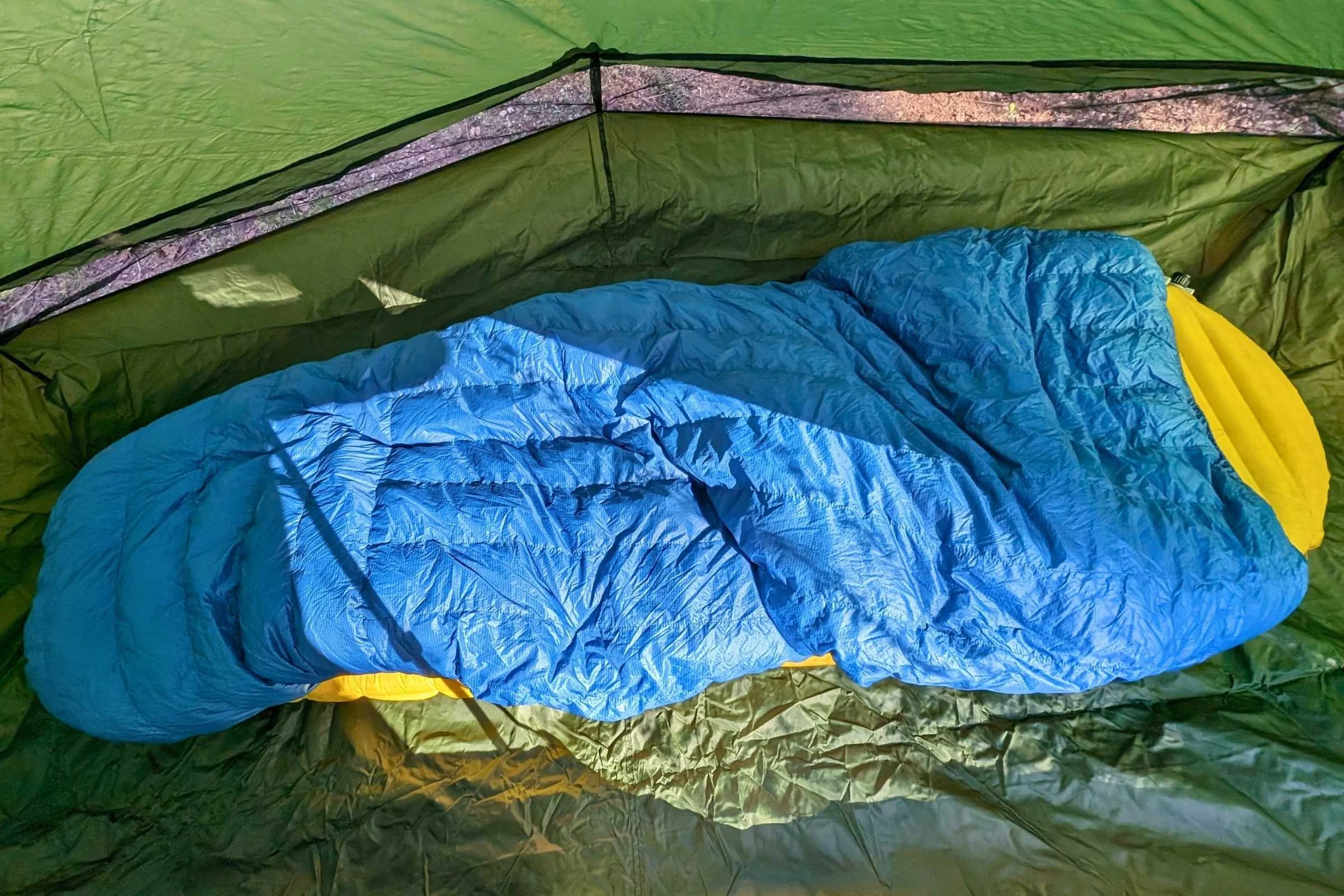 A green Six Moon Designs Lunar Solo tent pitched in a low-light forest setting.