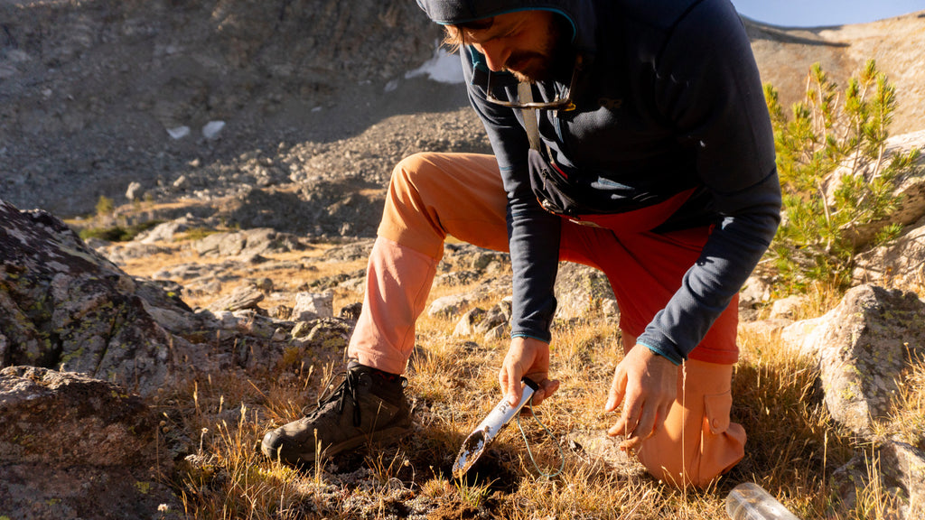 A person using a trowel to dig a hole in the forest floor.