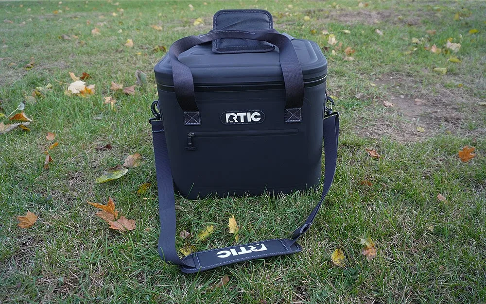 Black RTIC soft pack cooler sitting on a green lawn.
