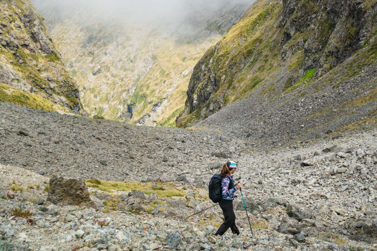 A fastpacker wearing protective running pants while traversing an alpine scree slope.