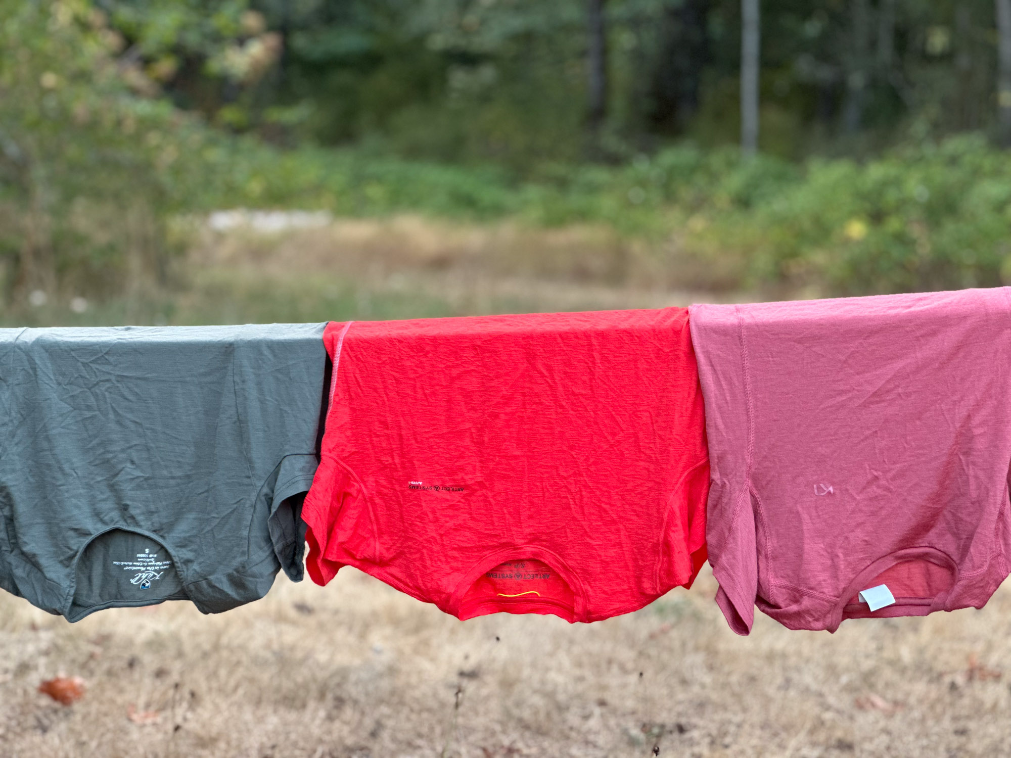A collection of different colored merino wool shirts laid out on rocks in a mountain setting.
