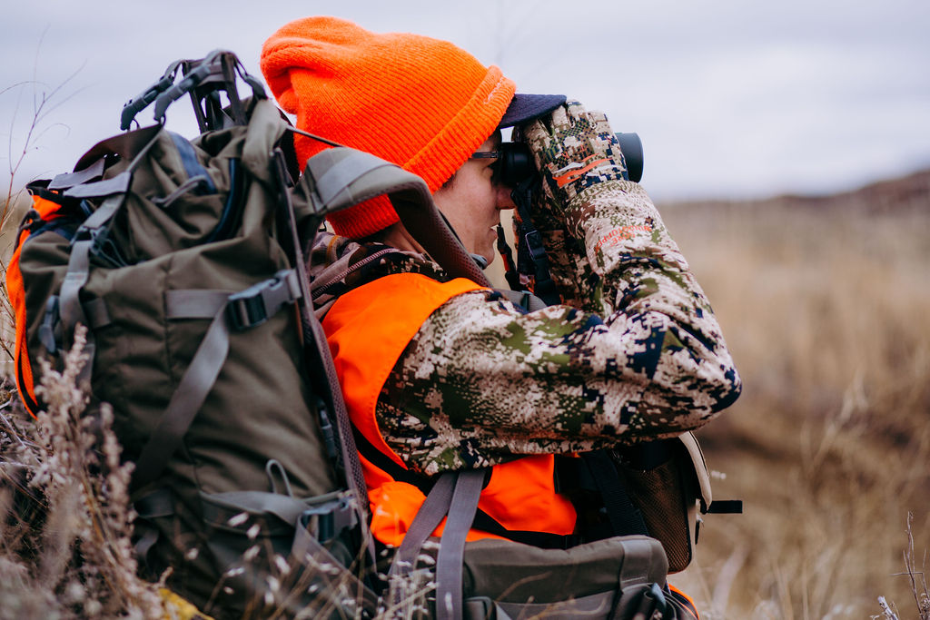 Two hunters in camouflage gear wearing tactical backpacks in a forest environment