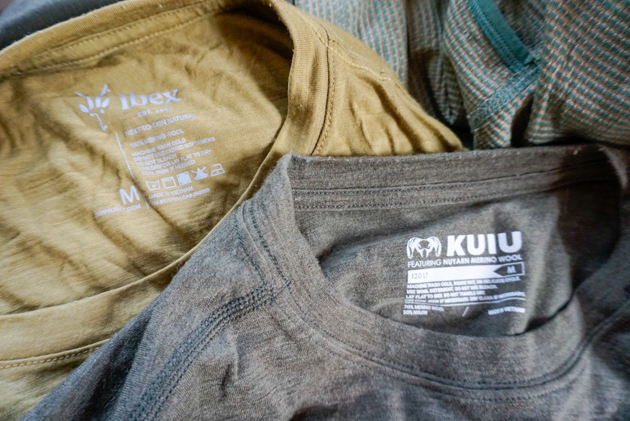 Several merino wool shirts from different brands laid flat for comparison.