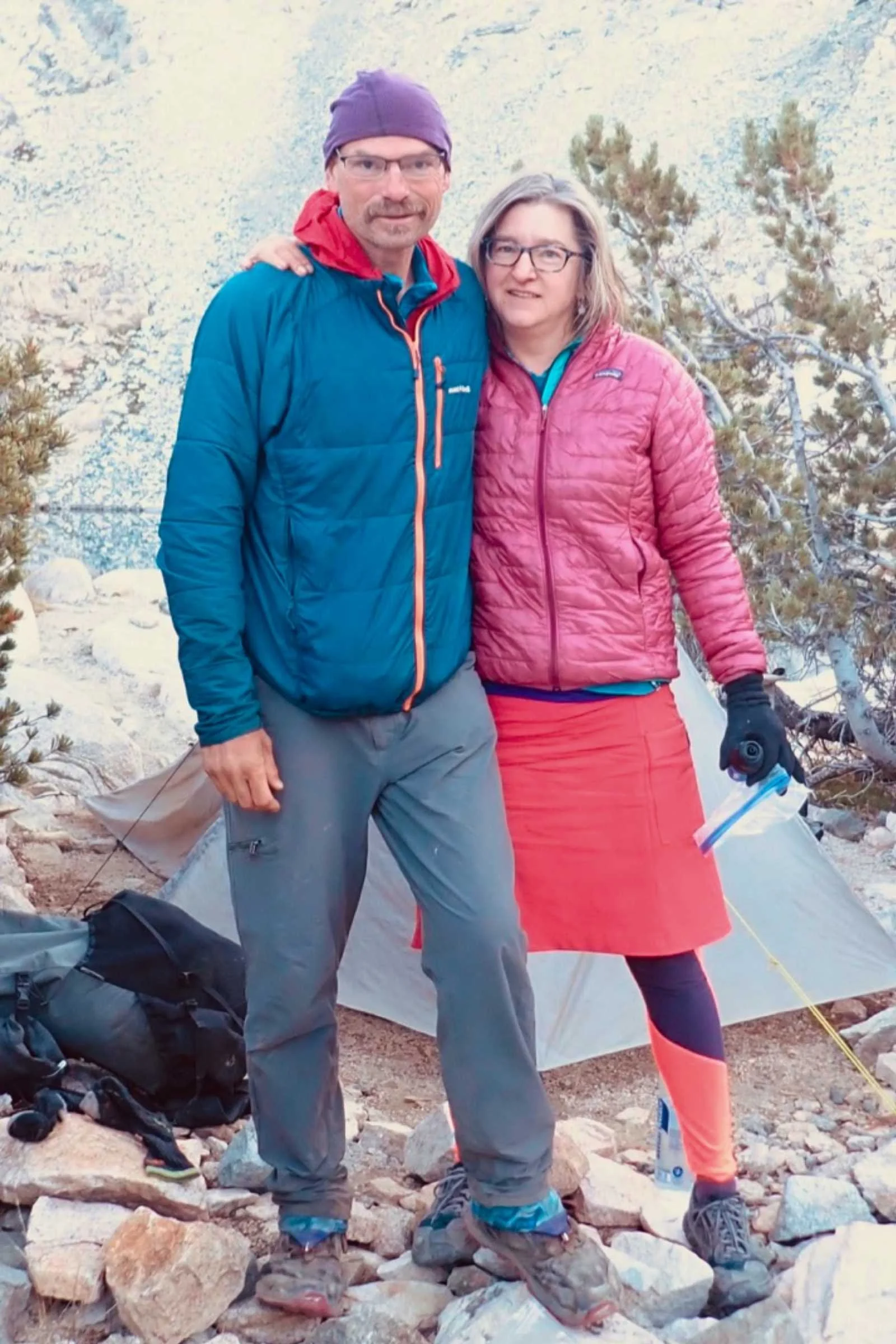 Two people wearing different synthetic jackets standing by a lake for testing