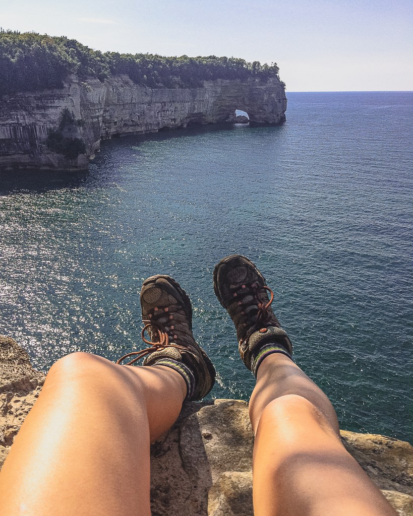 Hiker standing on a rocky cliff overlooking a vast lake and coastline.