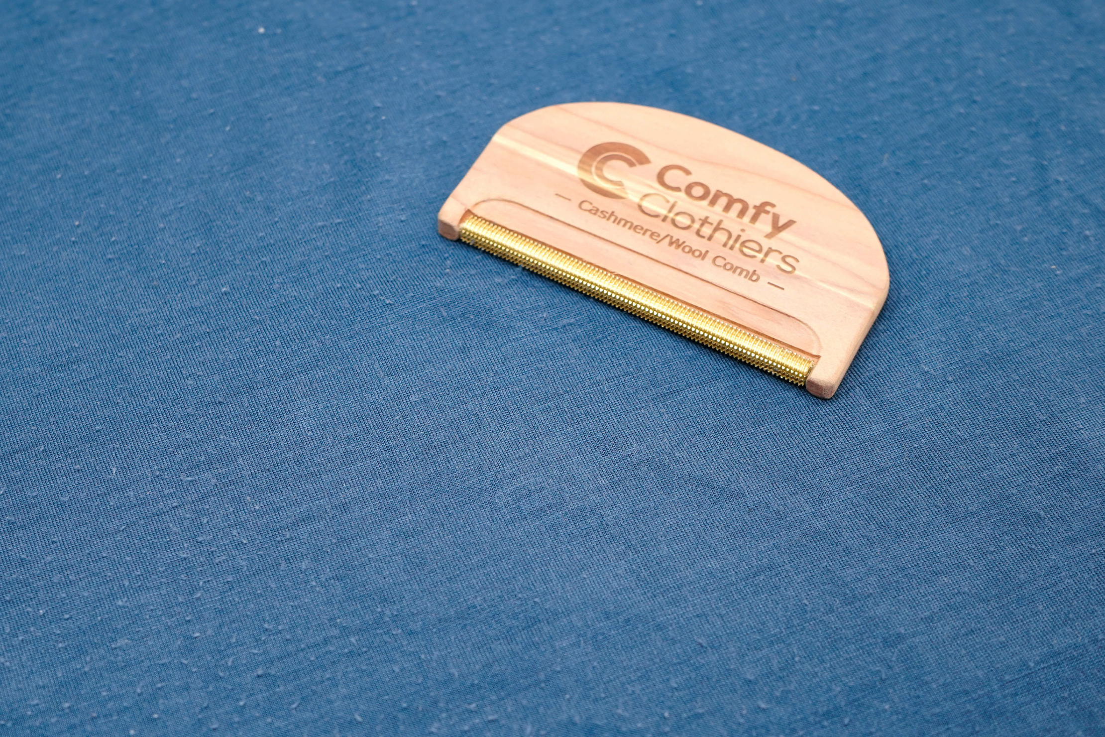 A close-up of a person using a fabric comb to remove pilling from a wool garment.
