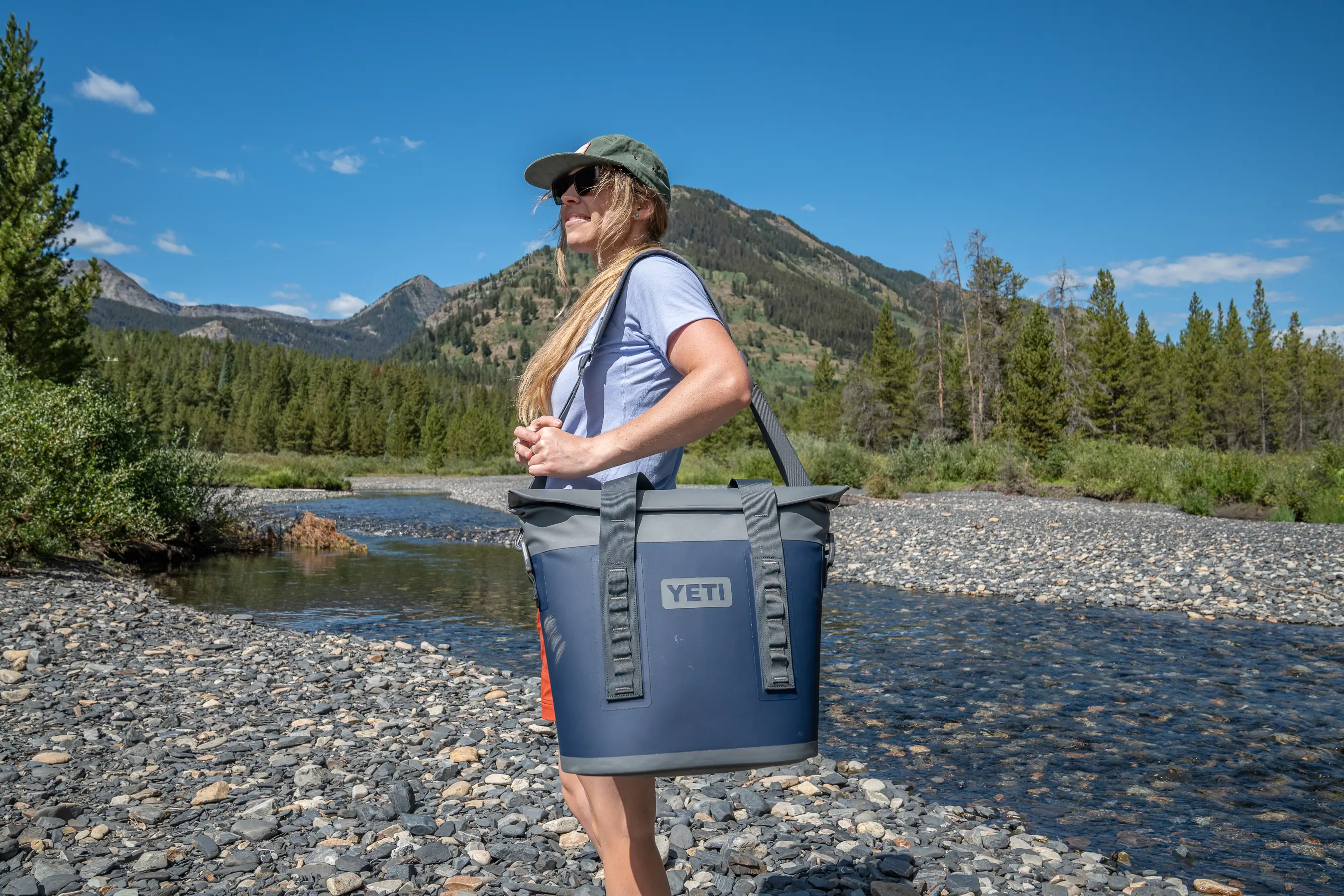 A woman carrying a grey soft cooler tote with a shoulder strap in an outdoor setting.