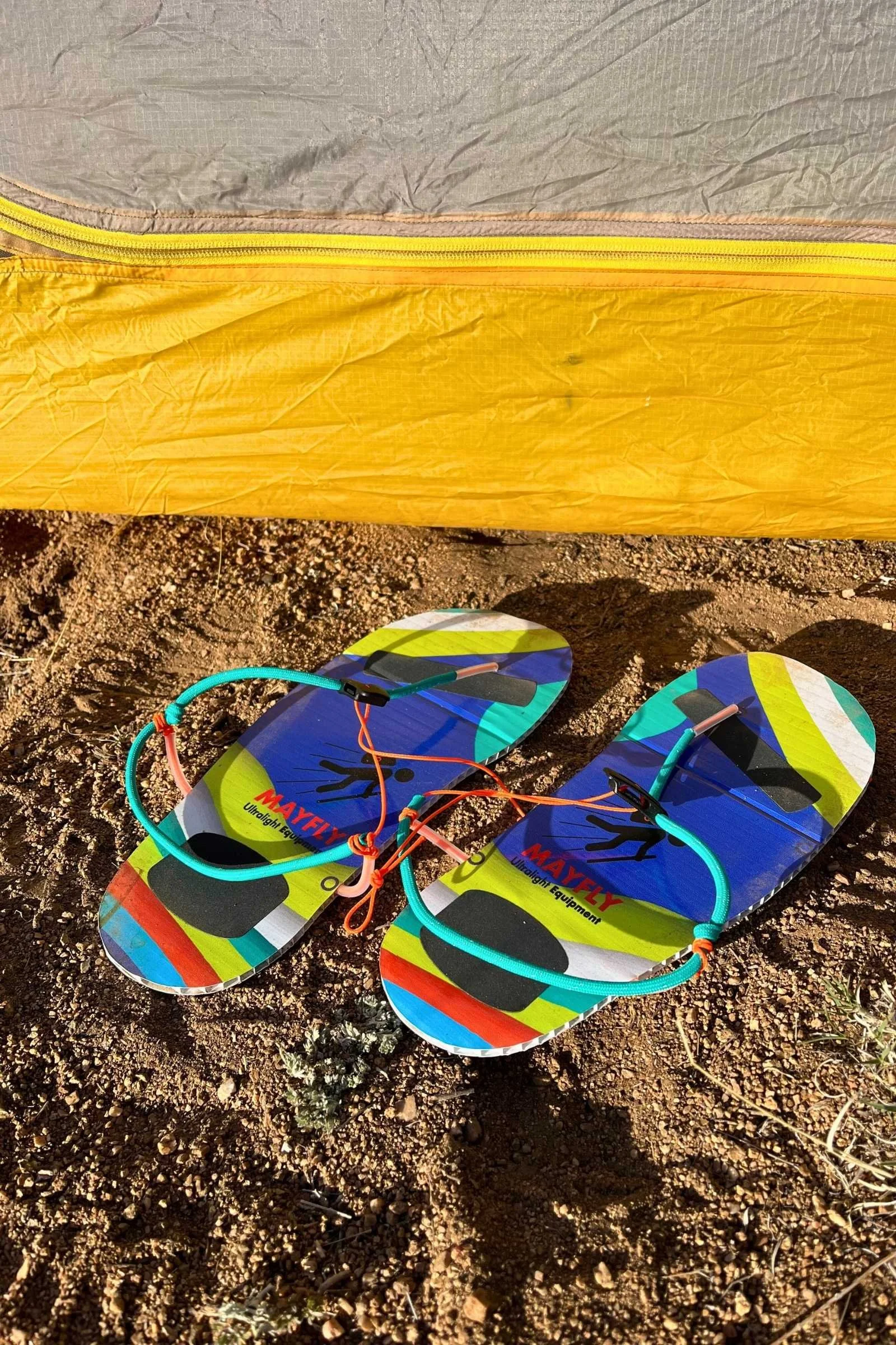 Ultra-minimalist Mayfly Imago sandals sitting on the ground outside a green tent.