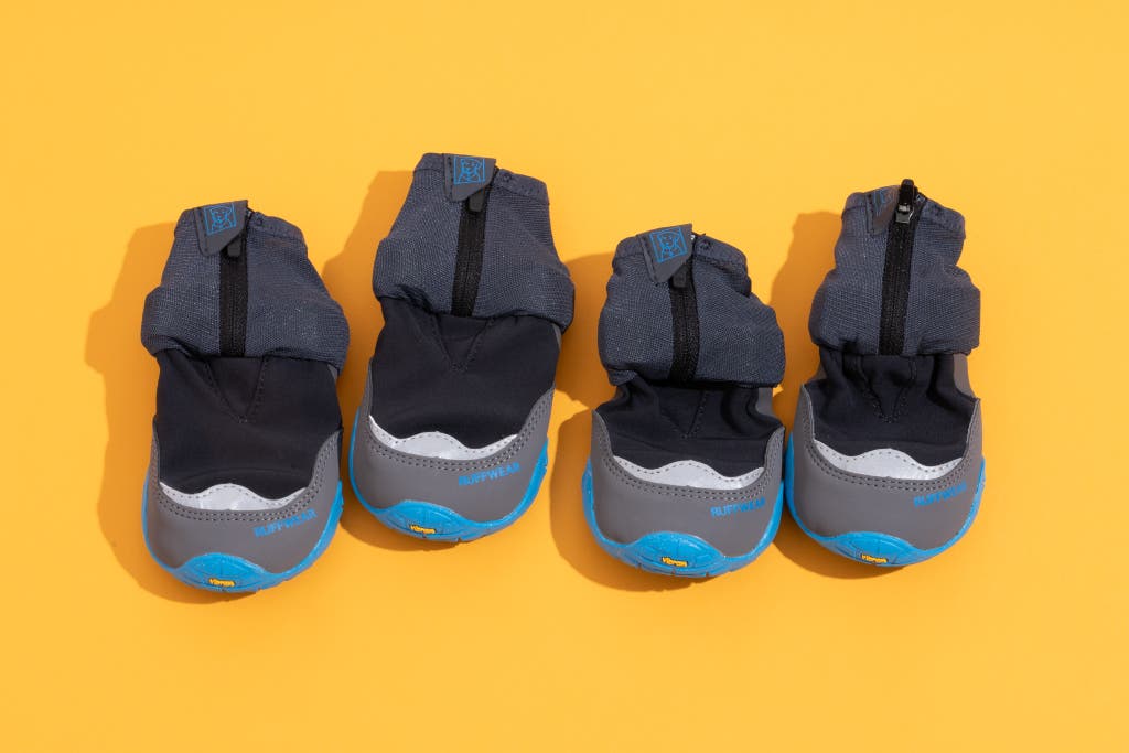 Four blue and black Ruffwear Polar Trex winter dog boots on a yellow background.