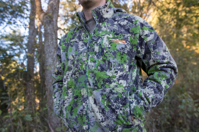 A hunter wearing a SITKA Stratus 2.0 Jacket near a wood line.