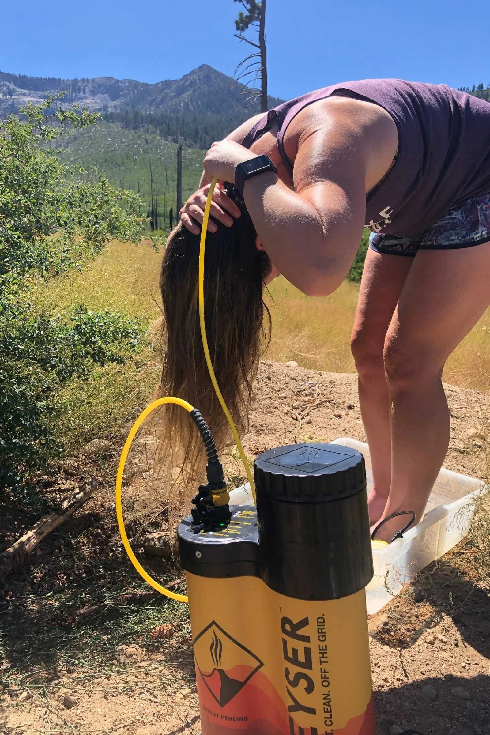 A person using the Geyser Systems heated camp shower nozzle to wash their hair.