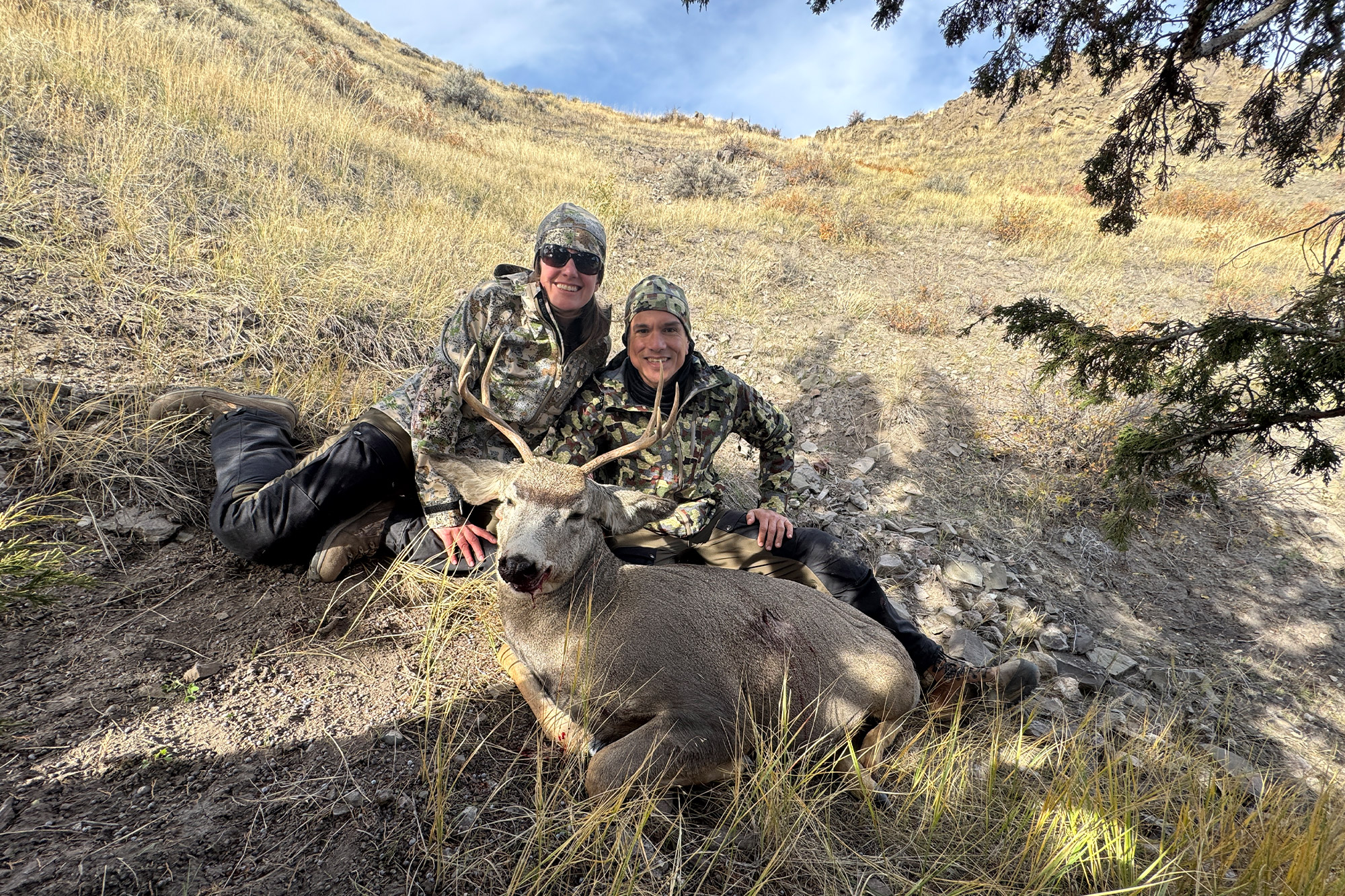 Two hunters in FORLOH gear posing with a harvested mule deer in the field.