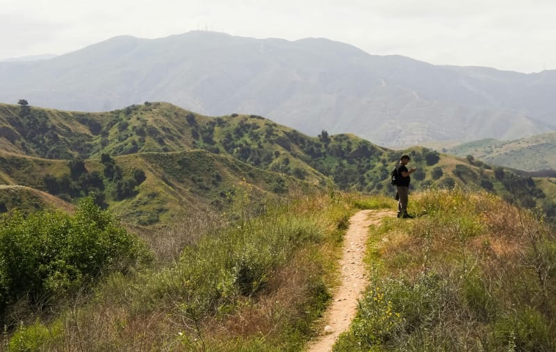 Hiker walking on a green trail with a lightweight backpack in a mountain landscape.