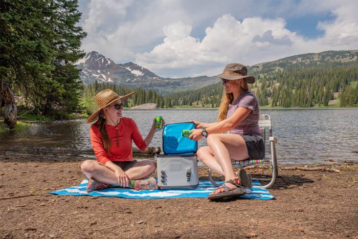Two women sitting by a lake with a soft cooler during a picnic.