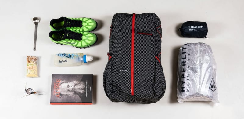 Flat lay of ultralight backpacking gear including pack, shoes, and stove.