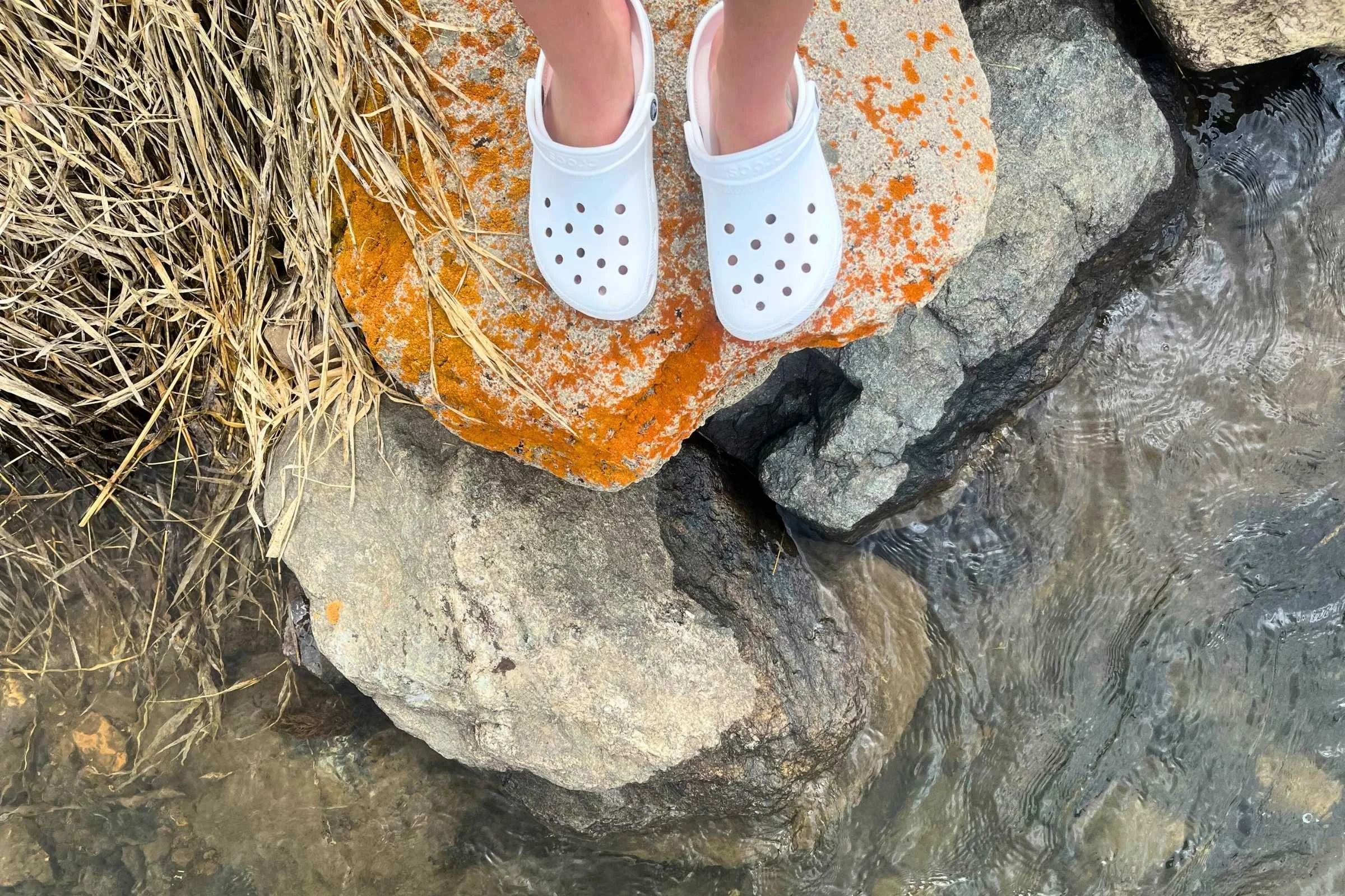 A person washing dirt off a pair of waterproof Crocs with water.