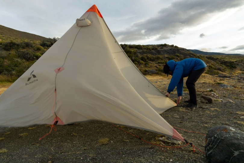 A hiker struggling against high winds while attempting to secure a mountaineering tent in Patagonia.